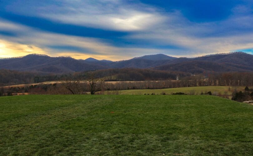 Rolling green hills at dusk with the Blue Ridge Mountains in the background under a dramatic cloudy sky, Virginia