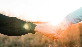 Two people holding hands outdoors at sunset, sunlight glowing through a golden field