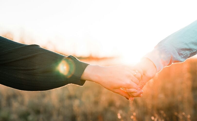 Two people holding hands outdoors at sunset, sunlight glowing through a golden field