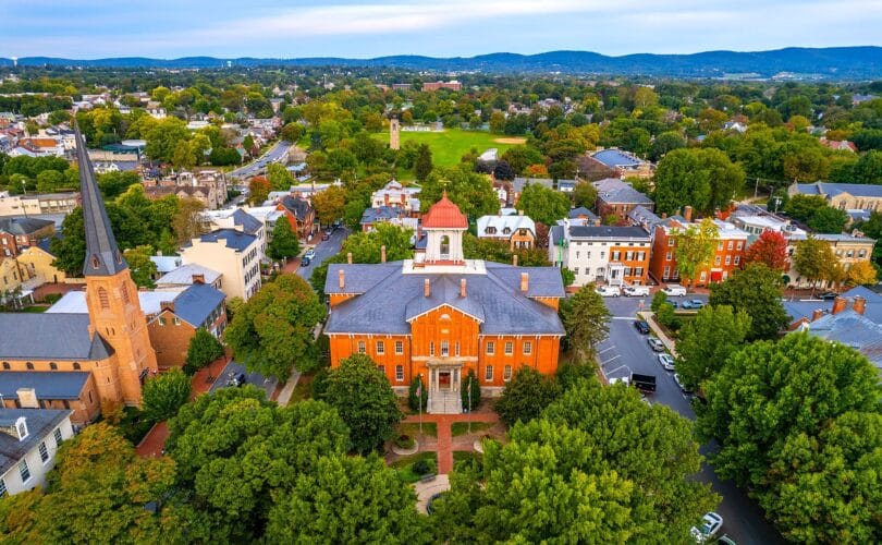 Aerial view of downtown Frederick, Maryland with historic brick buildings, church spires, and mountains in the distance