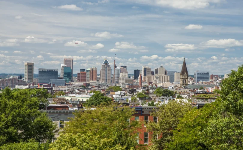Baltimore city skyline on a sunny day with rowhomes and trees in the foreground