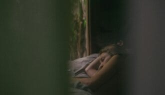 Grieving woman lying awake in bed at dawn, staring toward the window, unable to sleep