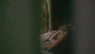 Grieving woman lying awake in bed at dawn, staring toward the window, unable to sleep