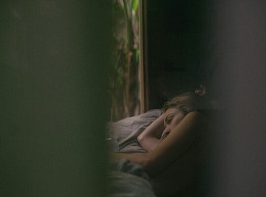 Grieving woman lying awake in bed at dawn, staring toward the window, unable to sleep