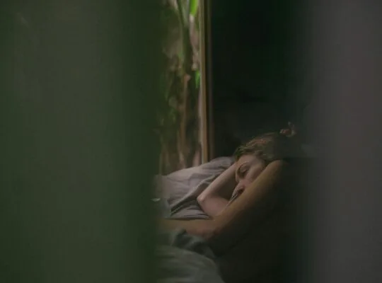 Grieving woman lying awake in bed at dawn, staring toward the window, unable to sleep