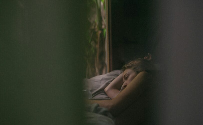 Grieving woman lying awake in bed at dawn, staring toward the window, unable to sleep