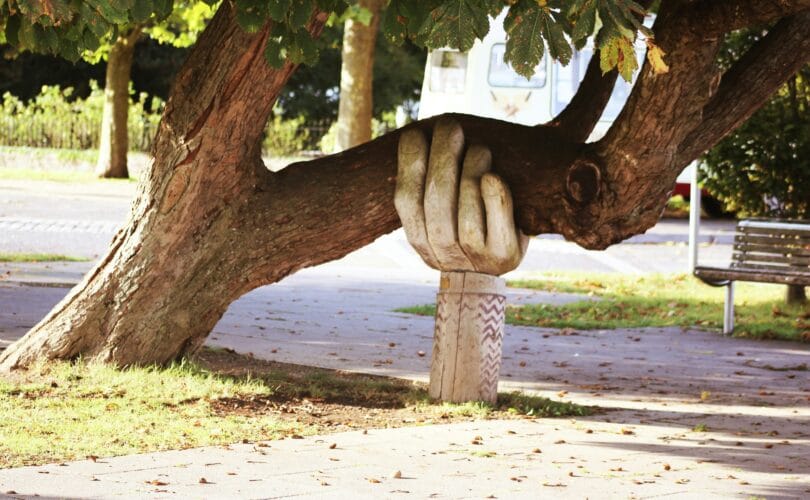 A carved wooden hand holding up a heavy tree branch, symbolizing support through grief.